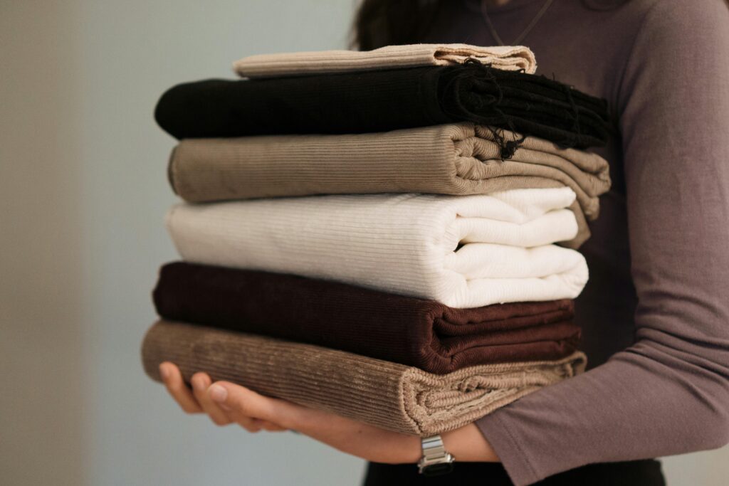 Close-up of hands holding a stack of folded neutral-toned fabrics, ideal for textile projects.